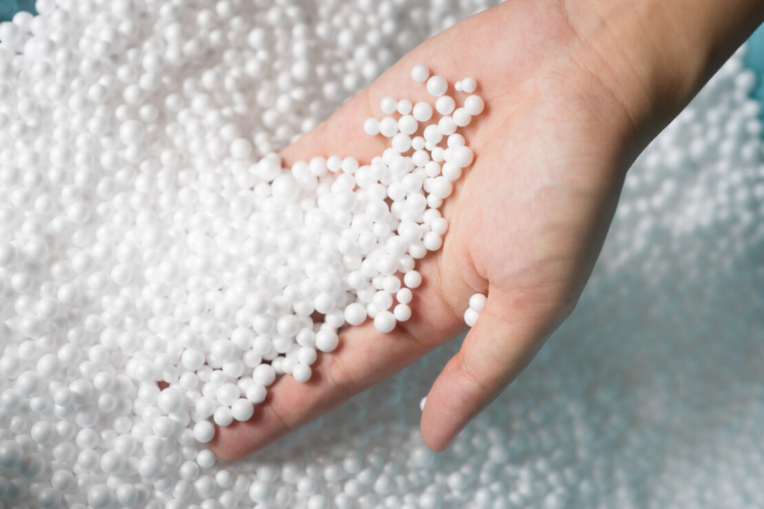 Small white polystyrene foam falling out of someone's palm into a pile of polystyrene granules